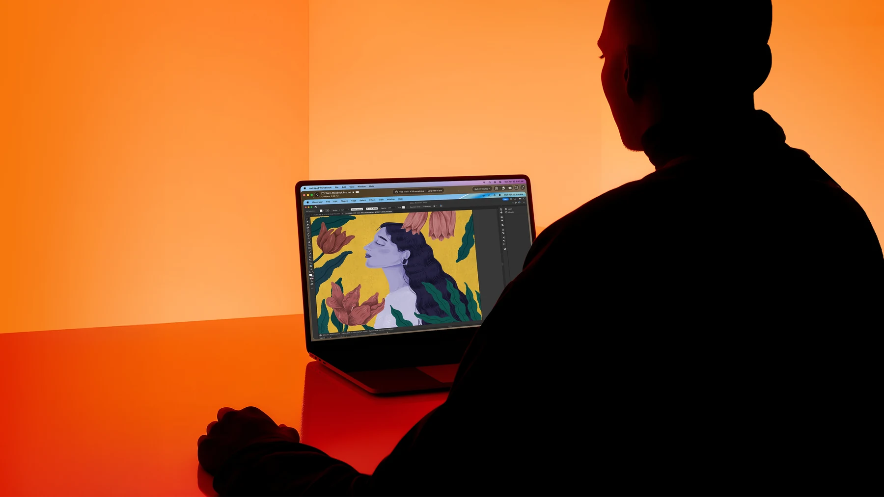 A designer at a MacBook in Astropad's orange studio light, working in an illustration app