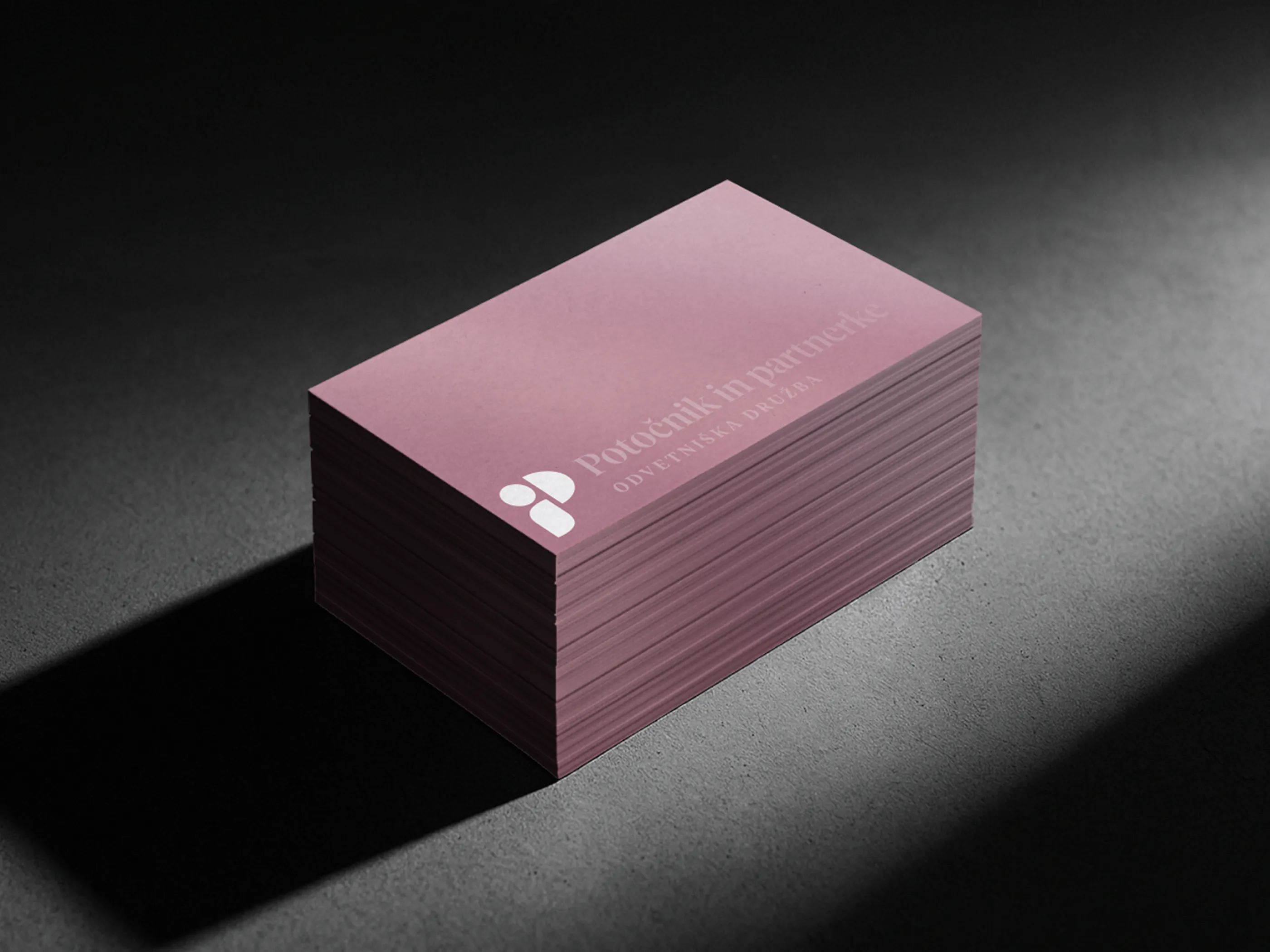 A stack of dusty pink business cards for Potocnik in partnerke on a dark surface in hard light, the firm's mark and name printed in white along the top card